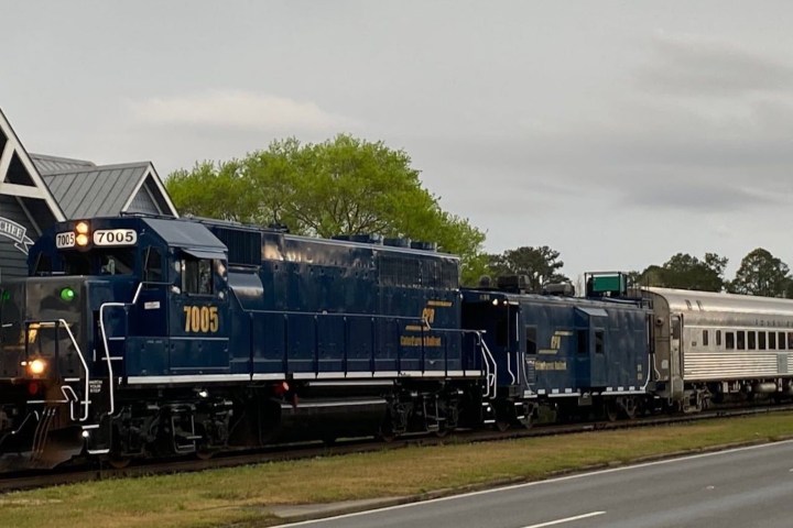 Blue train with several cars passing a small station building.